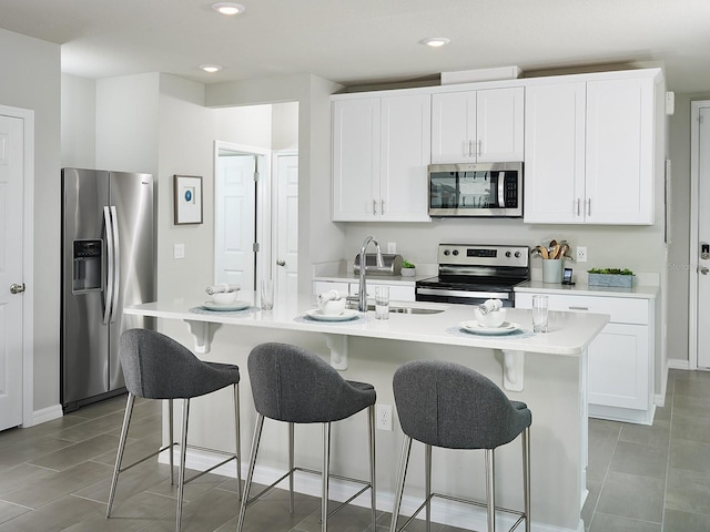 kitchen with stainless steel appliances, a kitchen island with sink, sink, and white cabinets