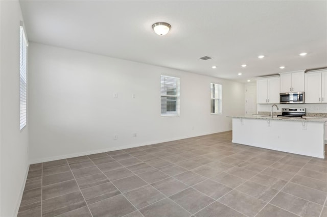 kitchen featuring sink, light stone counters, appliances with stainless steel finishes, a kitchen breakfast bar, and white cabinets