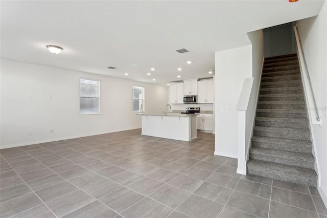 kitchen with white cabinetry, appliances with stainless steel finishes, a center island with sink, and light tile patterned floors