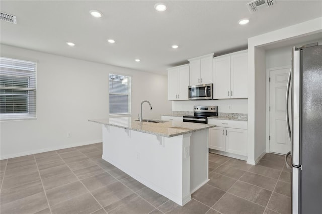 kitchen featuring sink, white cabinets, light stone counters, stainless steel appliances, and a center island with sink