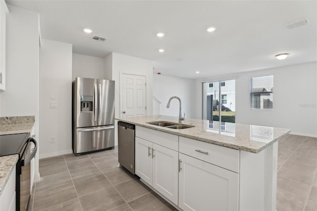 kitchen featuring sink, appliances with stainless steel finishes, white cabinetry, light stone countertops, and an island with sink