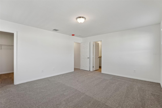 unfurnished bedroom featuring a walk in closet, light colored carpet, and a closet