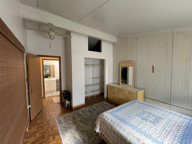 bedroom featuring ceiling fan, parquet floors, wooden walls, and ensuite bath