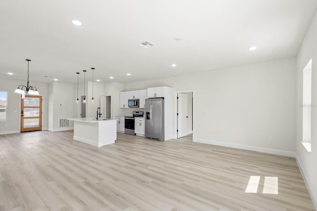 kitchen with appliances with stainless steel finishes, white cabinetry, light hardwood / wood-style floors, a center island with sink, and decorative light fixtures