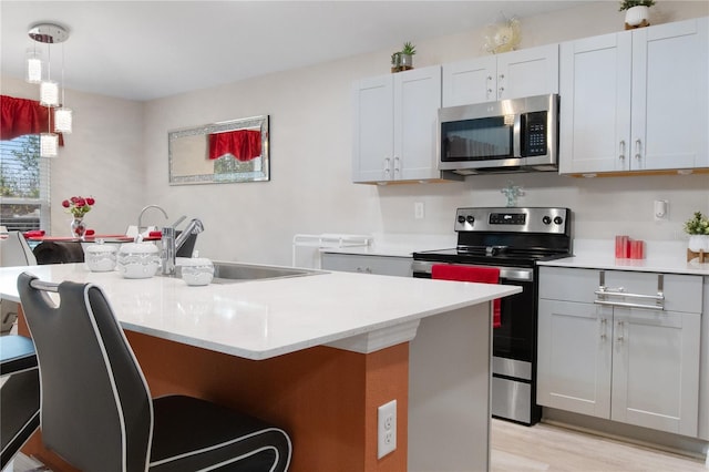 kitchen featuring pendant lighting, sink, light hardwood / wood-style flooring, stainless steel appliances, and an island with sink