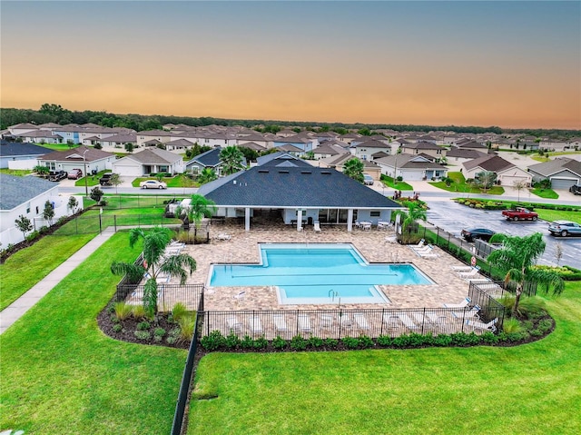 pool at dusk featuring a patio and a lawn