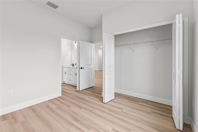 unfurnished bedroom featuring ensuite bathroom, a closet, and light hardwood / wood-style flooring