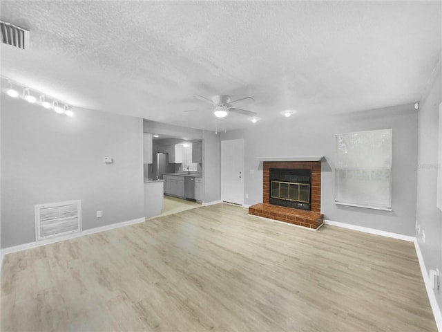 unfurnished living room with a brick fireplace, a textured ceiling, light hardwood / wood-style floors, and ceiling fan