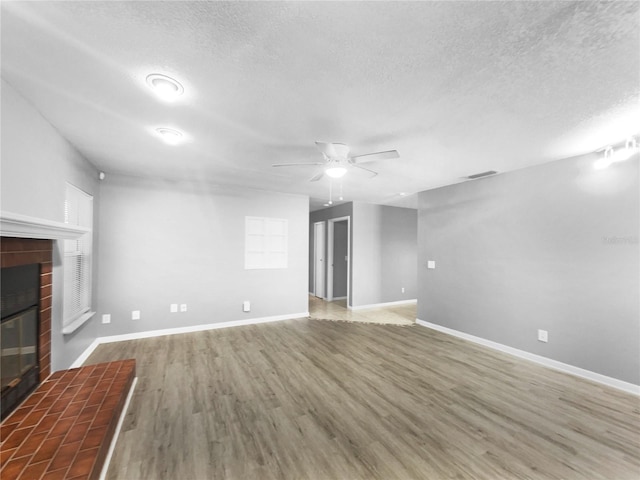 unfurnished living room with ceiling fan, hardwood / wood-style floors, a textured ceiling, and a fireplace