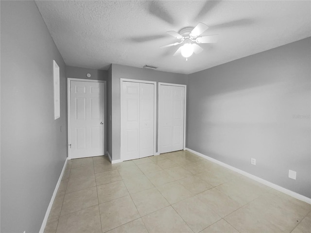 unfurnished bedroom with light tile patterned floors, a textured ceiling, ceiling fan, and two closets