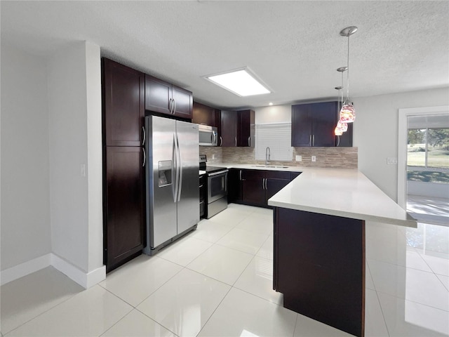 kitchen with appliances with stainless steel finishes, decorative light fixtures, tasteful backsplash, sink, and kitchen peninsula