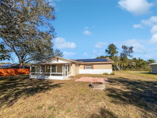 rear view of property featuring a yard, a fire pit, a sunroom, and solar panels