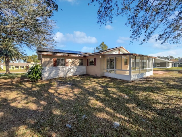 back of property with a lawn, a sunroom, and solar panels