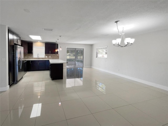 kitchen featuring light tile patterned flooring, stainless steel fridge, a notable chandelier, pendant lighting, and backsplash