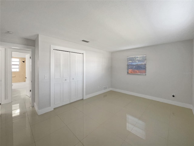 unfurnished bedroom featuring light tile patterned floors, ensuite bath, and a closet