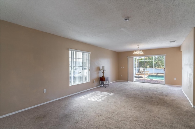 empty room featuring an inviting chandelier, a textured ceiling, and carpet flooring