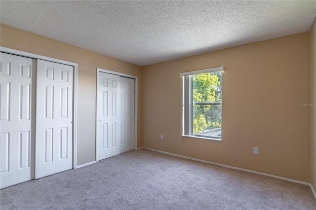 unfurnished bedroom featuring carpet, a textured ceiling, and two closets