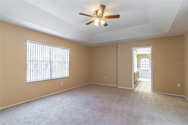 unfurnished room with ceiling fan, a raised ceiling, and light carpet