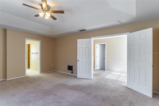 carpeted empty room featuring a raised ceiling, ceiling fan, and a textured ceiling