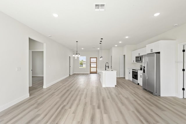 kitchen with light hardwood / wood-style flooring, appliances with stainless steel finishes, hanging light fixtures, white cabinets, and a center island with sink