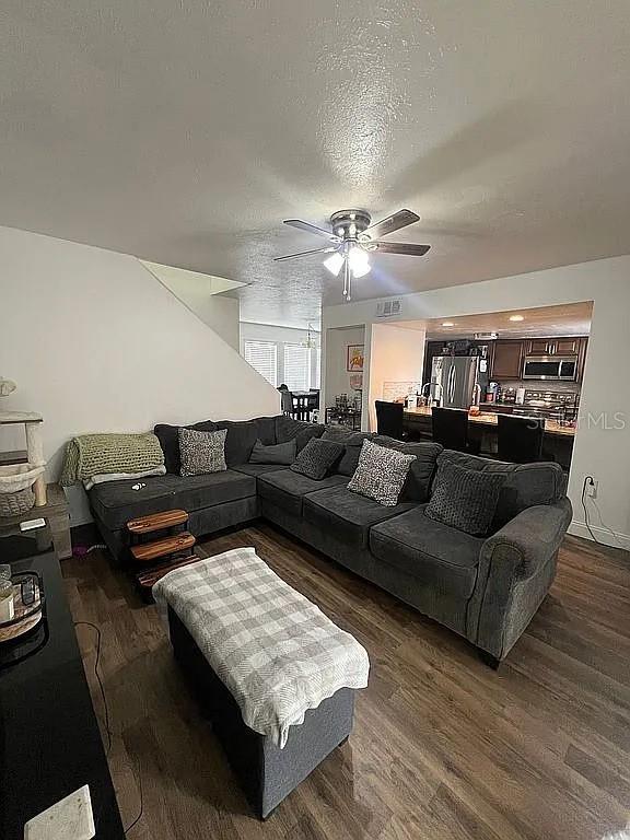 living room featuring ceiling fan, dark hardwood / wood-style floors, and a textured ceiling