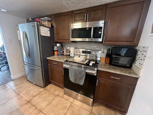 kitchen featuring stainless steel appliances, light tile patterned floors, dark brown cabinets, and backsplash