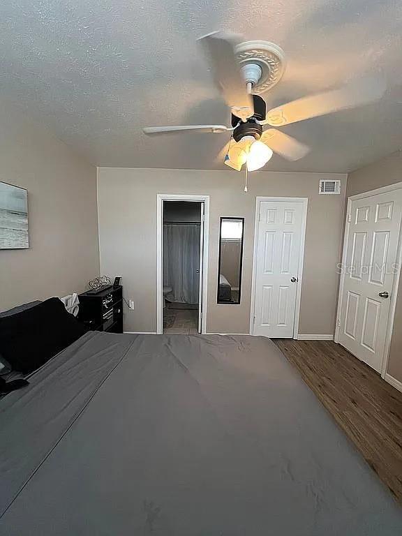 unfurnished bedroom with hardwood / wood-style floors, a textured ceiling, ceiling fan, and ensuite bath