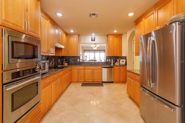 kitchen with backsplash, stainless steel appliances, sink, and dark stone countertops