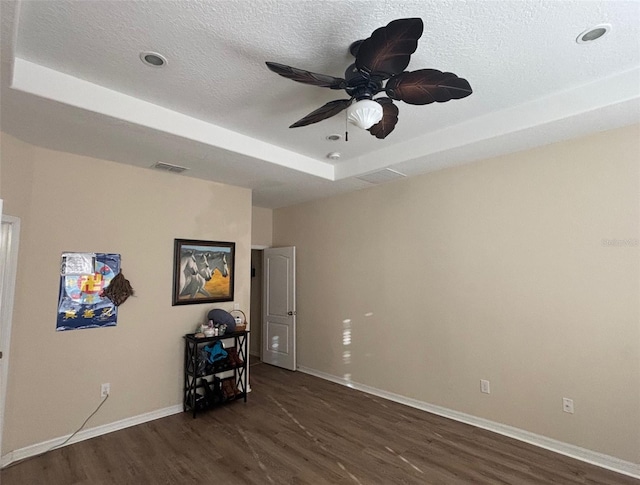 interior space with a raised ceiling, dark wood-type flooring, a textured ceiling, and ceiling fan