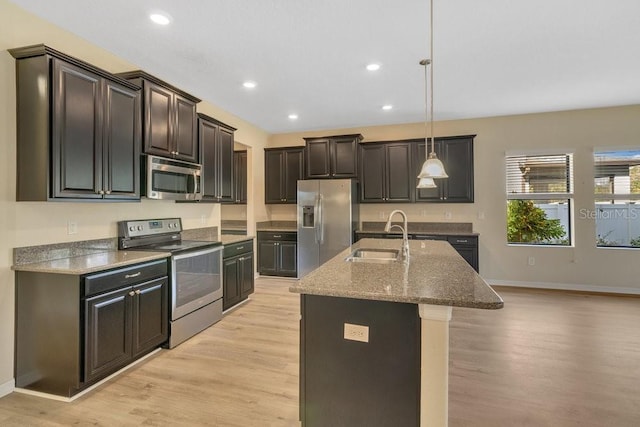 kitchen featuring appliances with stainless steel finishes, an island with sink, sink, hanging light fixtures, and light hardwood / wood-style floors