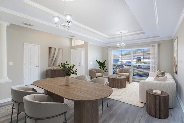 dining space featuring an inviting chandelier, a tray ceiling, and decorative columns