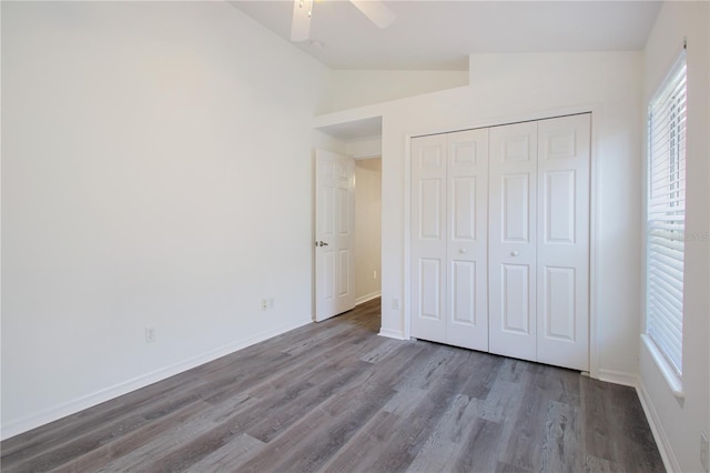 unfurnished bedroom with vaulted ceiling, dark hardwood / wood-style floors, multiple windows, ceiling fan, and a closet