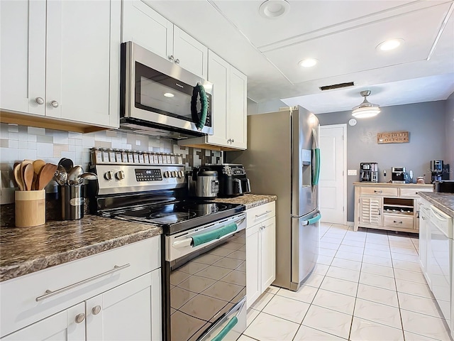 kitchen with light tile patterned floors, appliances with stainless steel finishes, white cabinetry, dark stone countertops, and decorative backsplash