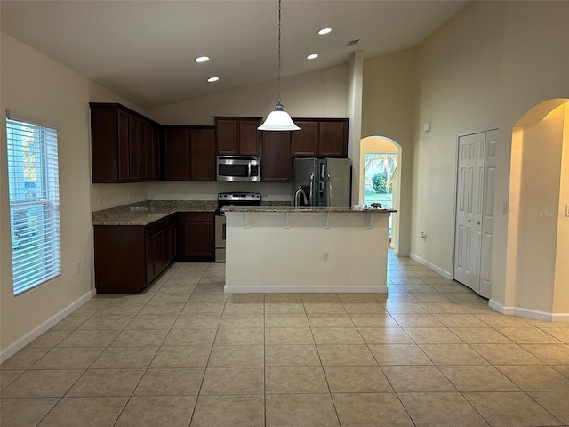 kitchen featuring appliances with stainless steel finishes, hanging light fixtures, light tile patterned floors, light stone countertops, and a center island with sink