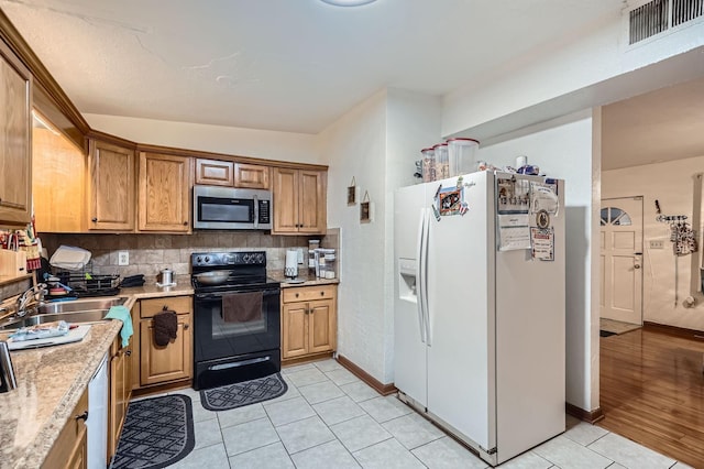 kitchen featuring light tile patterned flooring, appliances with stainless steel finishes, tasteful backsplash, sink, and light stone counters