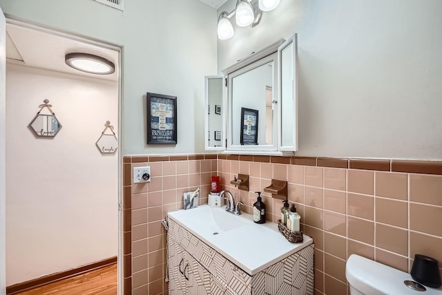 bathroom with wood-type flooring, tile walls, vanity, and toilet