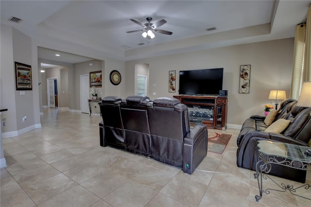 living room with light tile patterned flooring, ceiling fan, and a tray ceiling