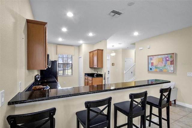 kitchen featuring a kitchen breakfast bar, dark stone counters, hanging light fixtures, light tile patterned floors, and kitchen peninsula