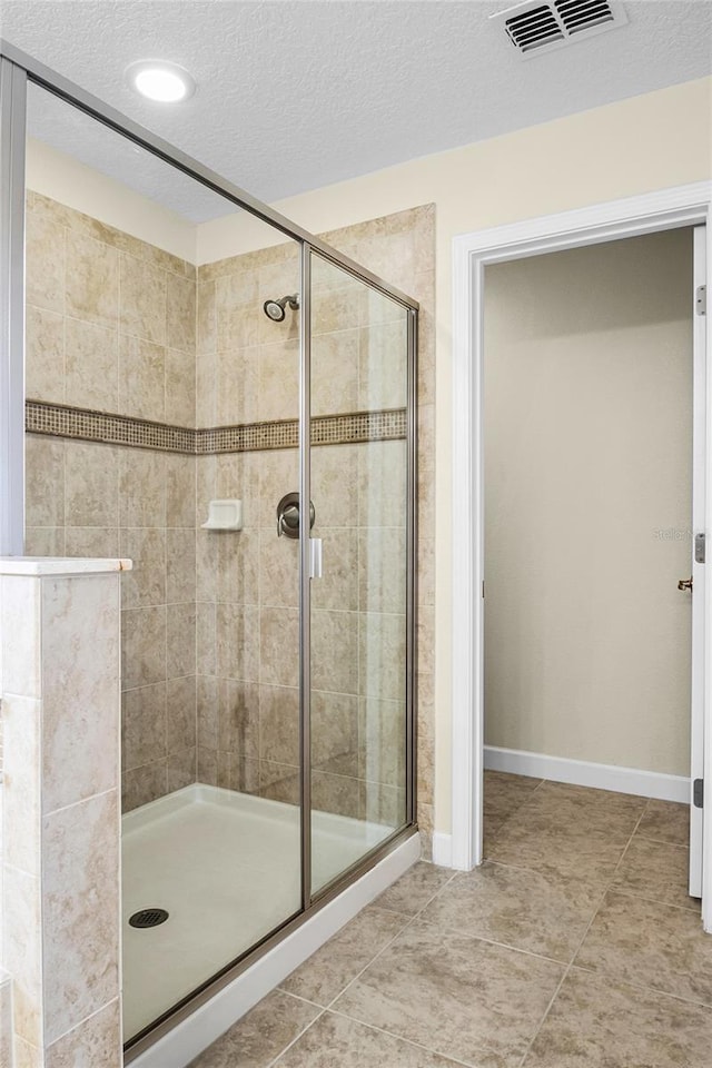 bathroom featuring tile patterned flooring, a shower with door, and a textured ceiling