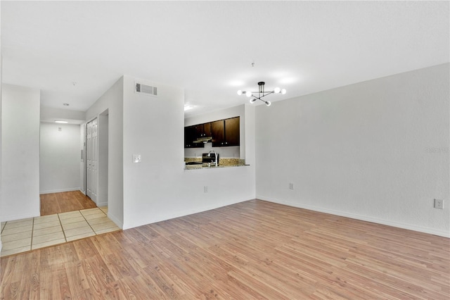 unfurnished living room with an inviting chandelier and light wood-type flooring