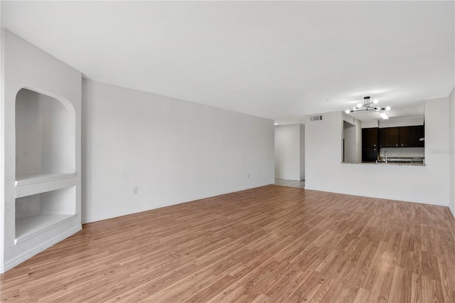 unfurnished living room featuring an inviting chandelier and light hardwood / wood-style flooring