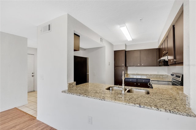 kitchen with light stone counters, appliances with stainless steel finishes, kitchen peninsula, and sink