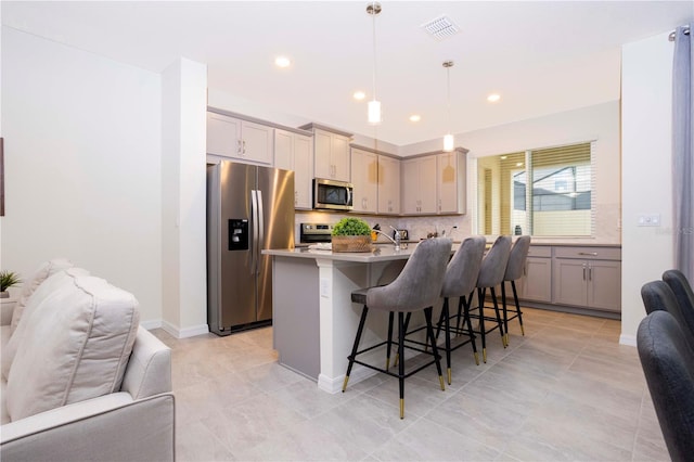 kitchen featuring a kitchen bar, decorative light fixtures, appliances with stainless steel finishes, a kitchen island with sink, and backsplash