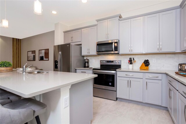 kitchen with a kitchen bar, sink, appliances with stainless steel finishes, pendant lighting, and backsplash