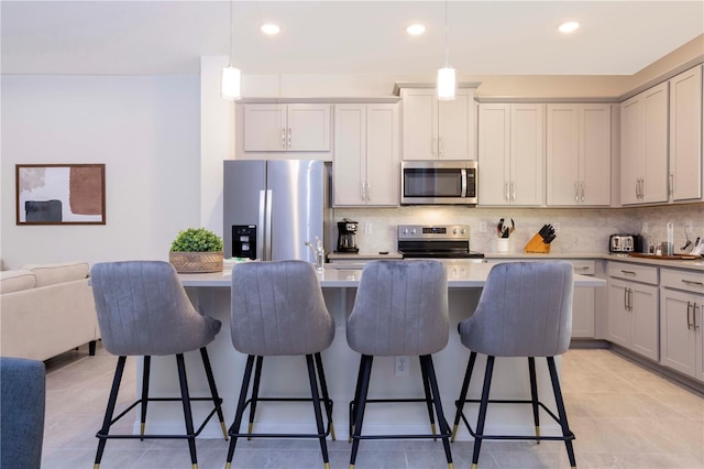 kitchen with a breakfast bar, appliances with stainless steel finishes, hanging light fixtures, backsplash, and an island with sink