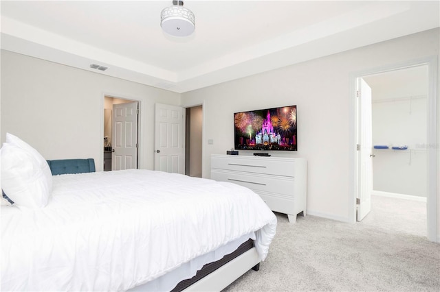 bedroom featuring light carpet, a tray ceiling, and a walk in closet