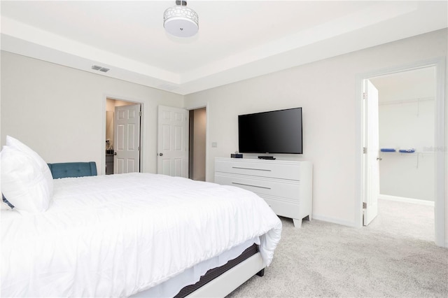 carpeted bedroom featuring a raised ceiling and a walk in closet