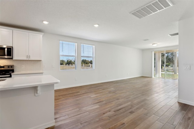 kitchen with a breakfast bar area, stainless steel appliances, light hardwood / wood-style floors, white cabinets, and decorative backsplash