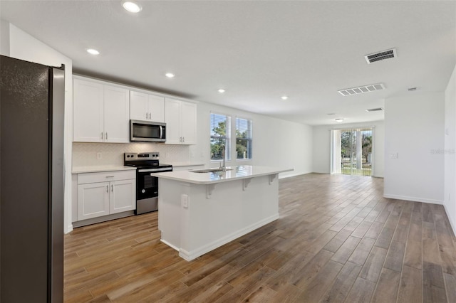 kitchen with appliances with stainless steel finishes, light hardwood / wood-style flooring, a center island with sink, and white cabinets