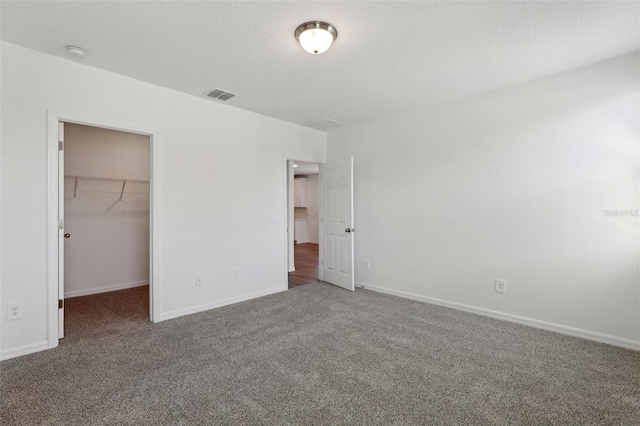 unfurnished bedroom featuring dark carpet, a closet, a textured ceiling, and a spacious closet